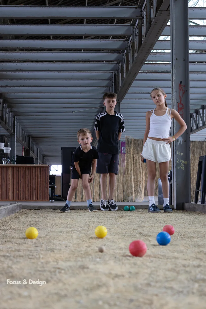Drie kinderen spelen petanque op een overdekte baan tijdens een kinderfeestje van Bougez