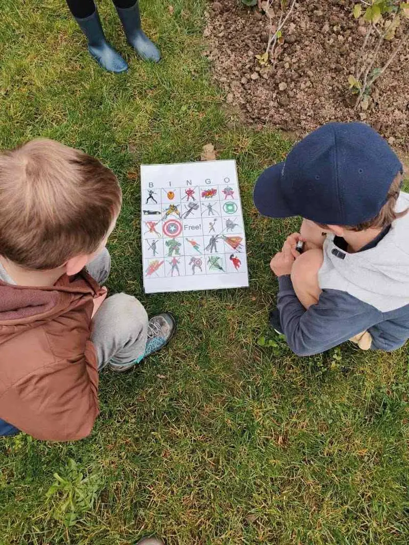 Twee jongens bestuderen hun bingokaart zittend in het gras tijdens een buitenspel van Bougez
