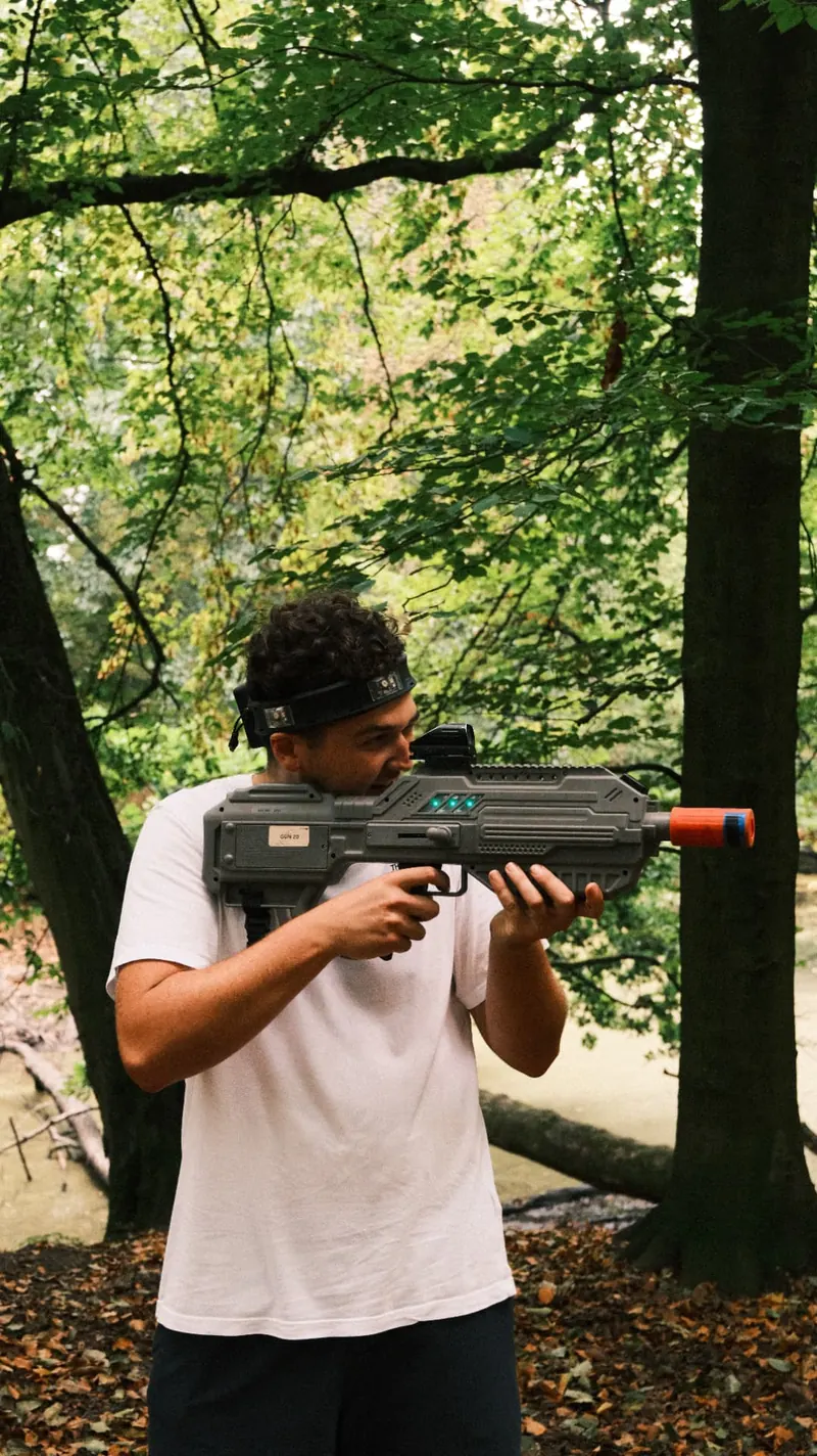 Deelnemer richt met een lasergeweer tussen de bomen tijdens een lasershoot van Bougez