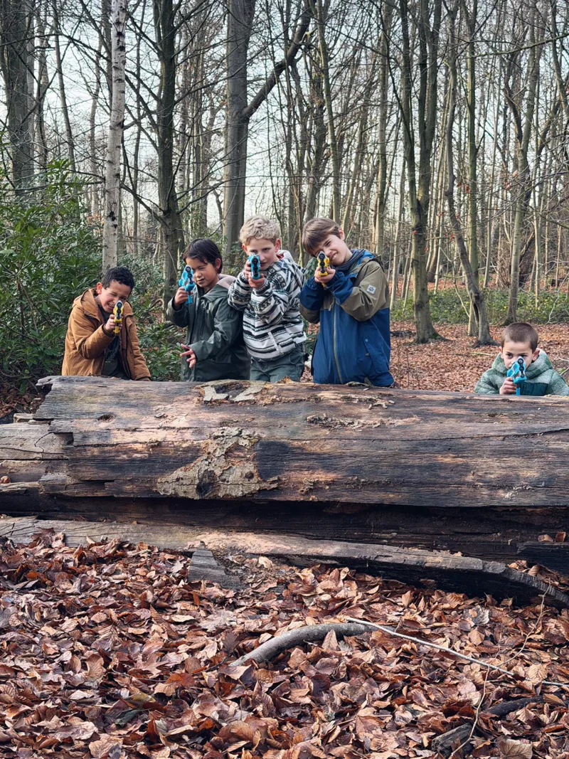 Vijf kinderen richten met hun lasergeweer vanachter een boomstam tijdens een lasershoot van Bougez