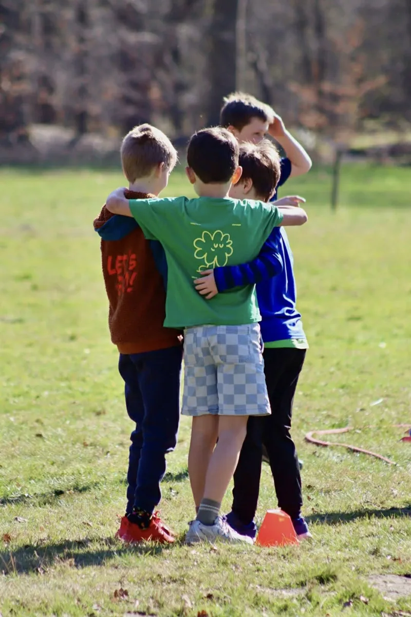 Vier jongens staan arm in arm in het gras tijdens een kinderfeestje van Bougez
