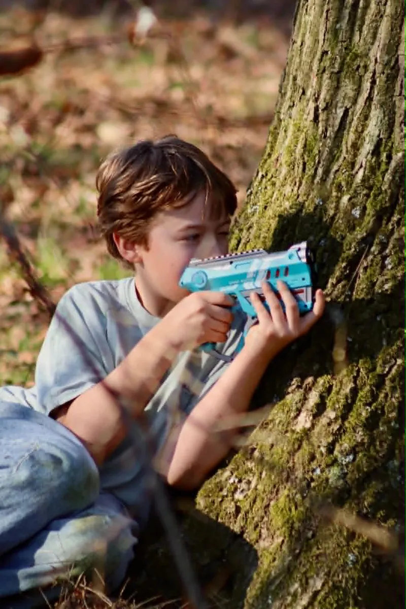 Jongen richt met een lasergeweer vanachter een boom op een kinderfeestje van Bougez