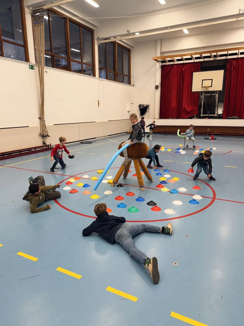 Kinderen spelen een spel met gekleurde hoedjes in de sporthal tijdens een kinderfeestje van Bougez