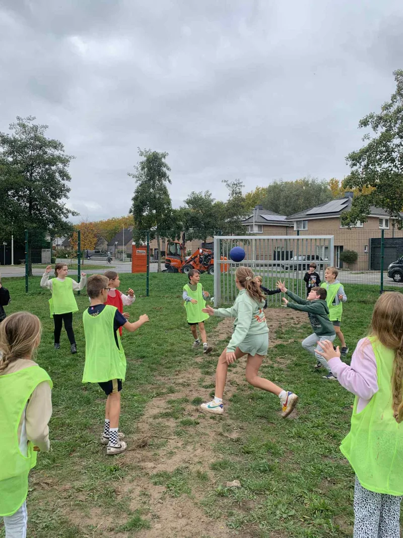 Kinderen met fluogele hesjes spelen een balspel op het veld tijdens een kinderfeestje van Bougez