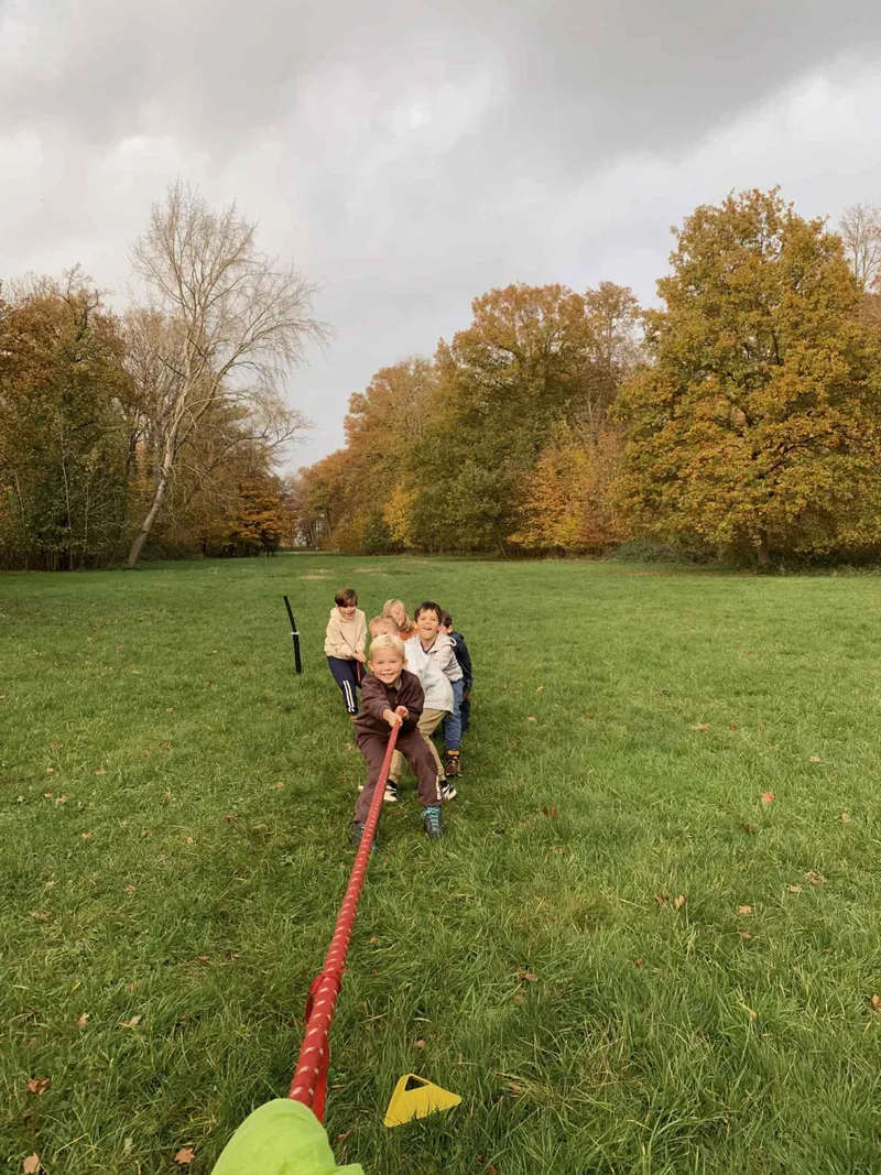Kinderen trekken samen aan een rood touw tijdens touwtrekken op een grasveld bij Bougez
