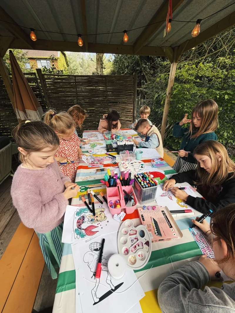 Groep kinderen tekent samen aan een lange tafel tijdens een creatief kinderfeestje van Bougez