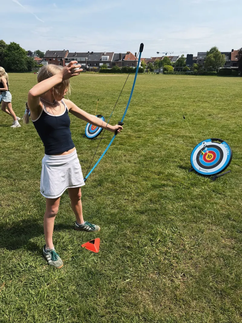 Meisje richt met pijl en boog op het veld tijdens een kinderfeestje van Bougez